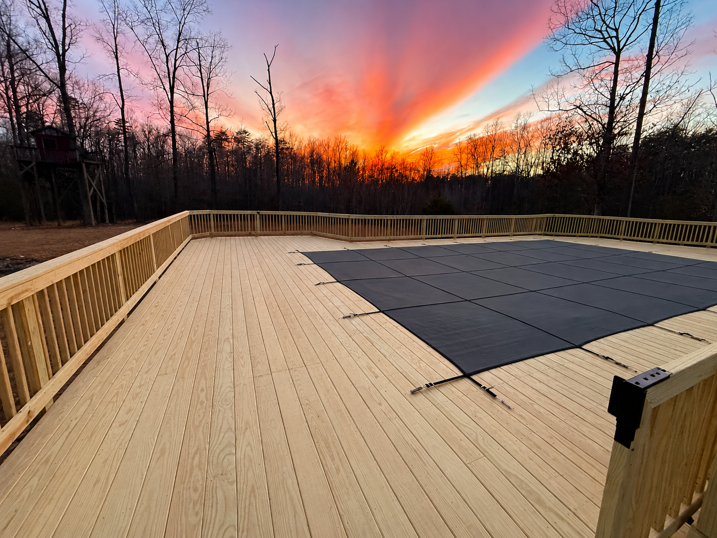 Custom wood deck with railings and in-ground pool cover at sunset